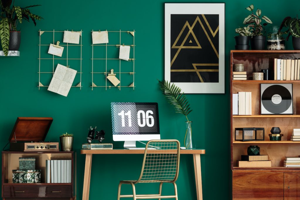 Green home office interior with a computer on the desk, wooden cabinet and poster on the wall, decorating with emerald green
